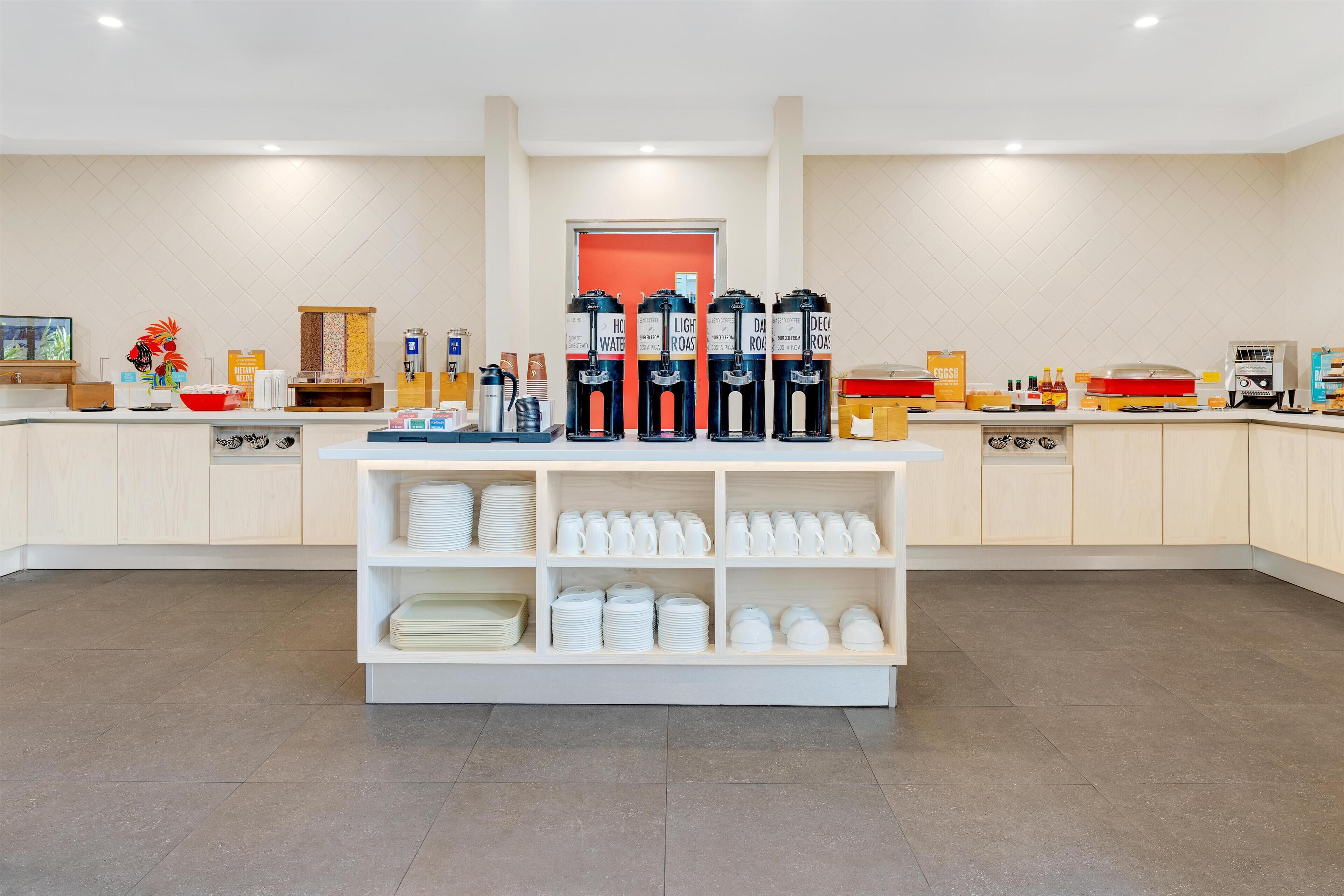 A buffet area with coffee dispensers, a fruit bowl, and neatly arranged plates and bowls.