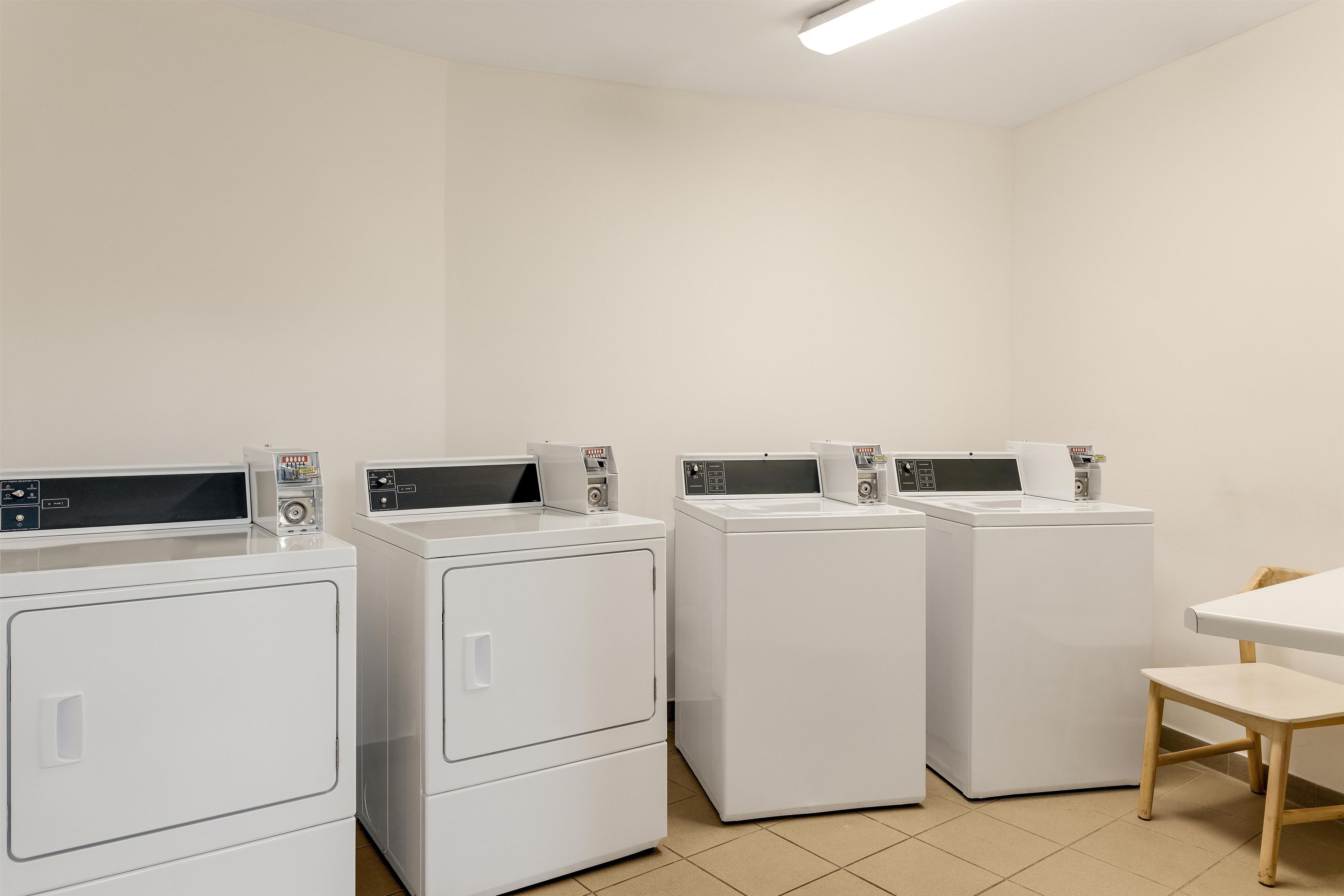 A laundry room with four white front-loading washing machines and a wooden chair.