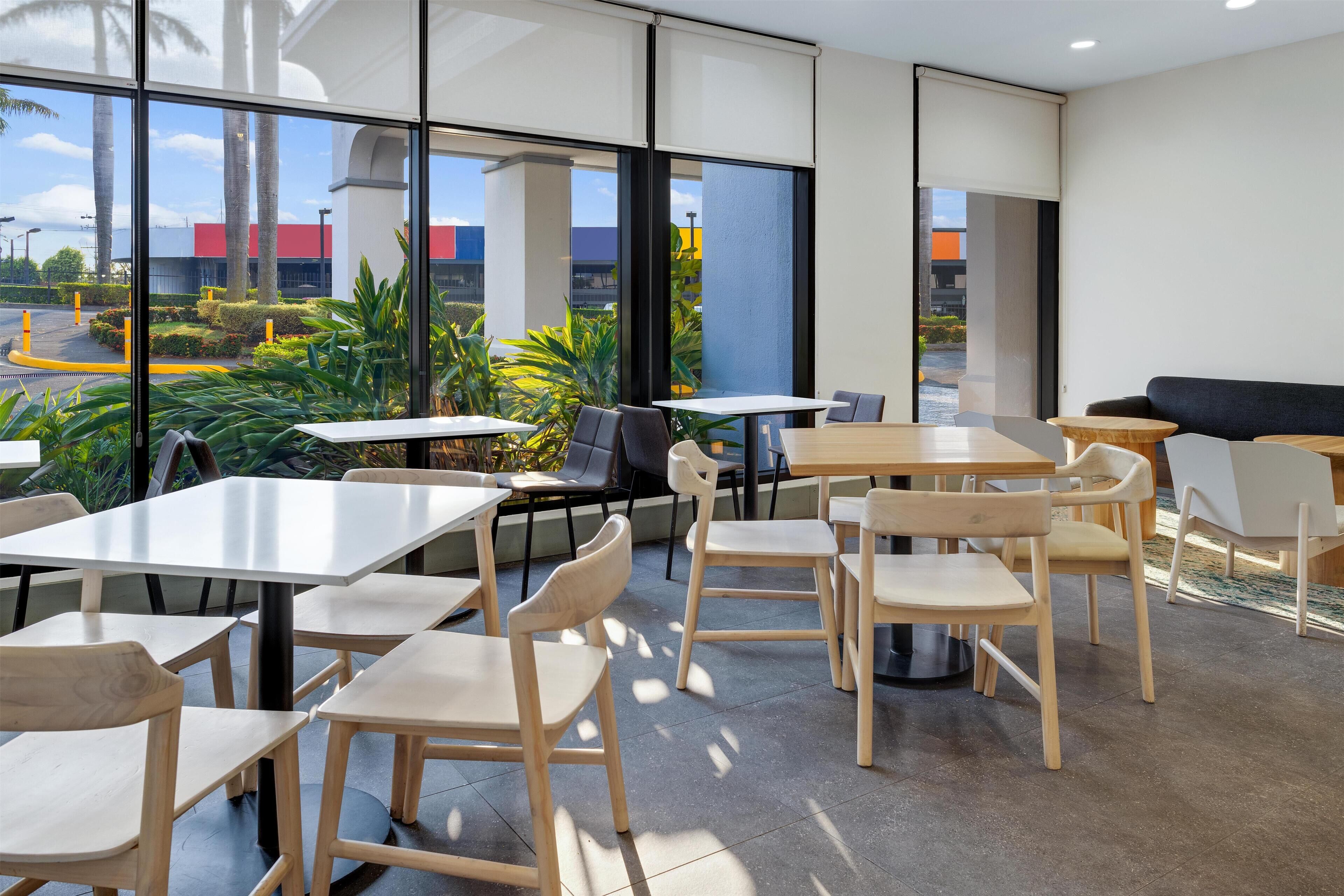 A modern indoor seating area with tables and chairs, large windows, and a view of the outside.