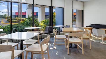 A modern indoor seating area with tables and chairs, large windows, and a view of the outside.