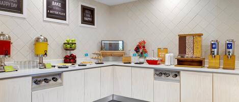 Una cocina moderna con armarios blancos, microondas integrado y espacio para café.