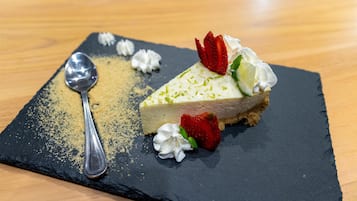 Una porción de pastel de queso sobre un plato de pizarra, con crema batida y fresas.