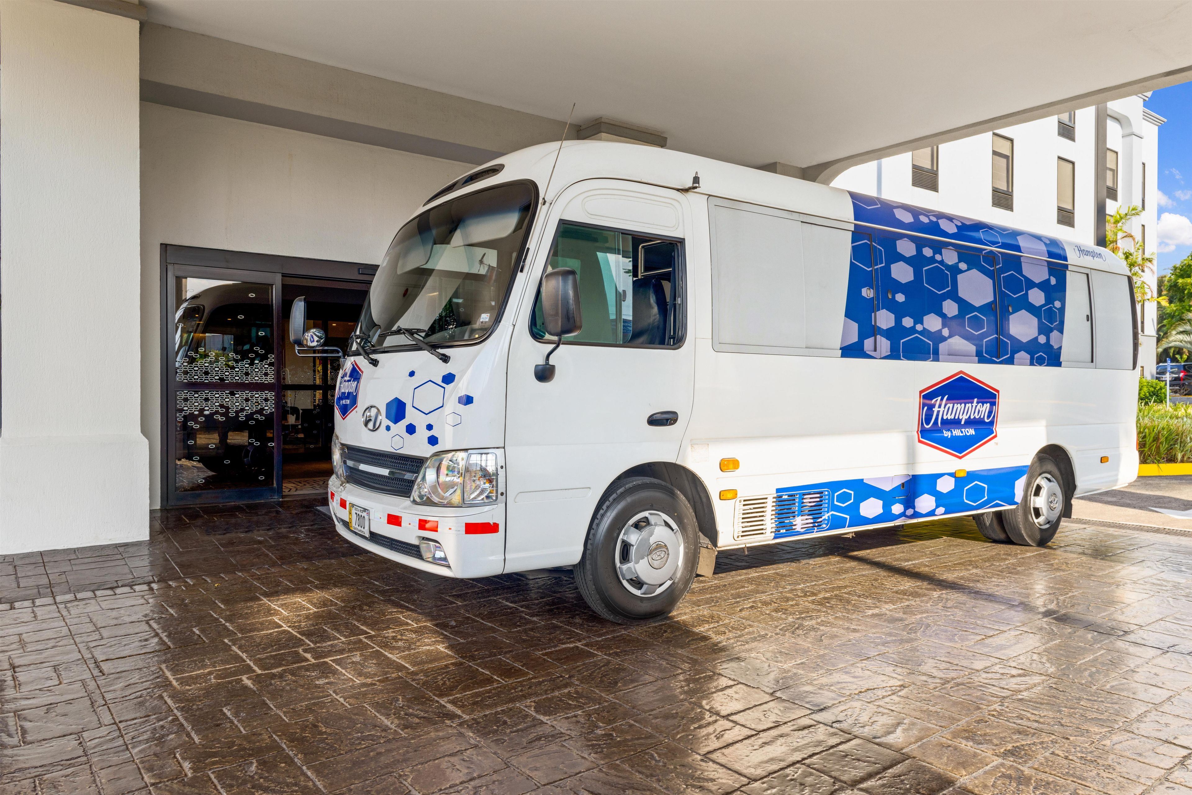 A white and blue Hampton by Hilton van parked outside a building with a tiled entrance.