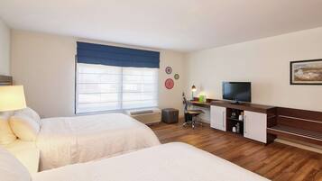 A hotel room with two beds, a desk with a chair, a television, and a window with a blue curtain.