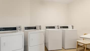 A laundry room with four white washing machines, a chair, and a table.
