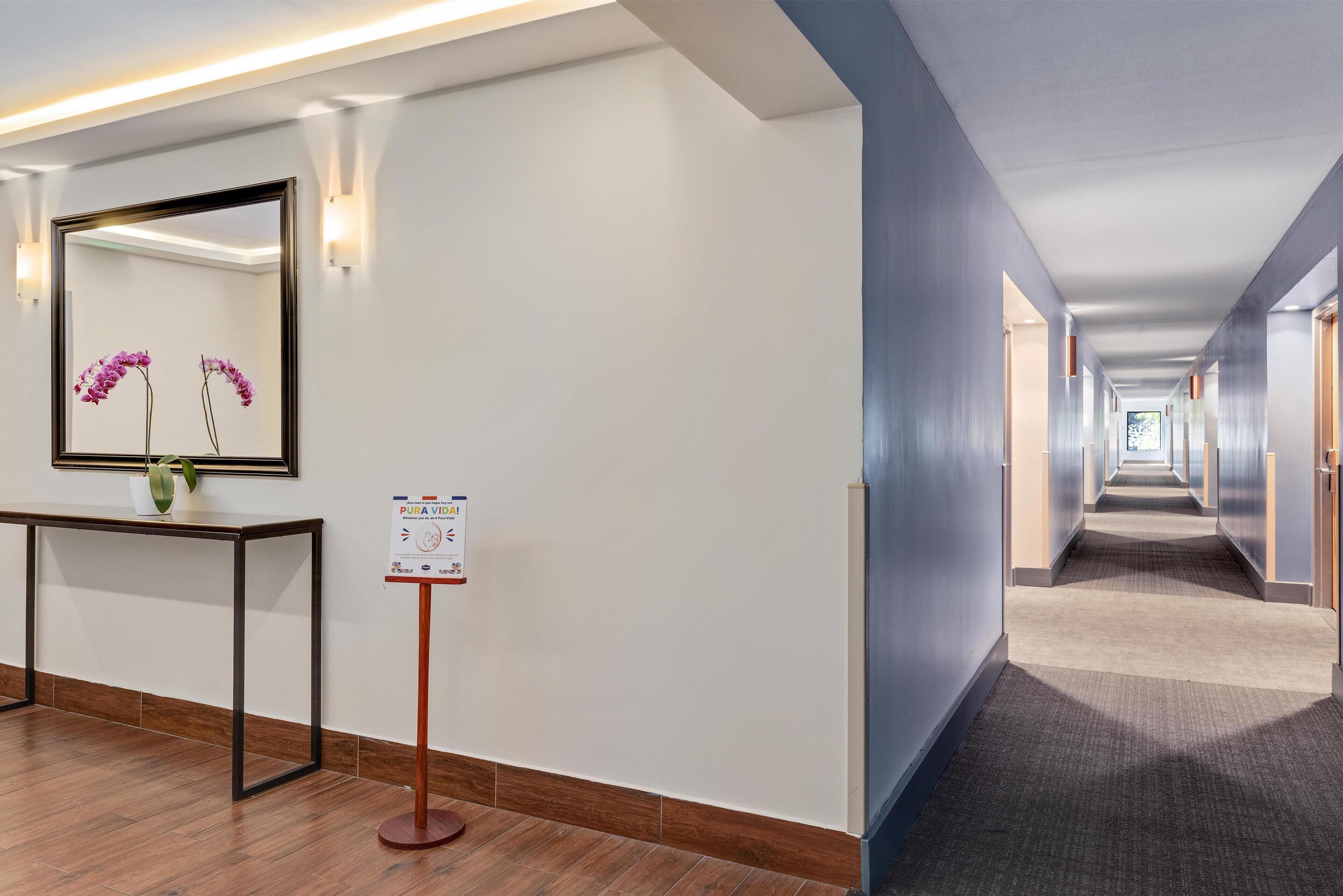A hotel corridor with a reception desk, a mirror, a sign, and a carpeted floor.