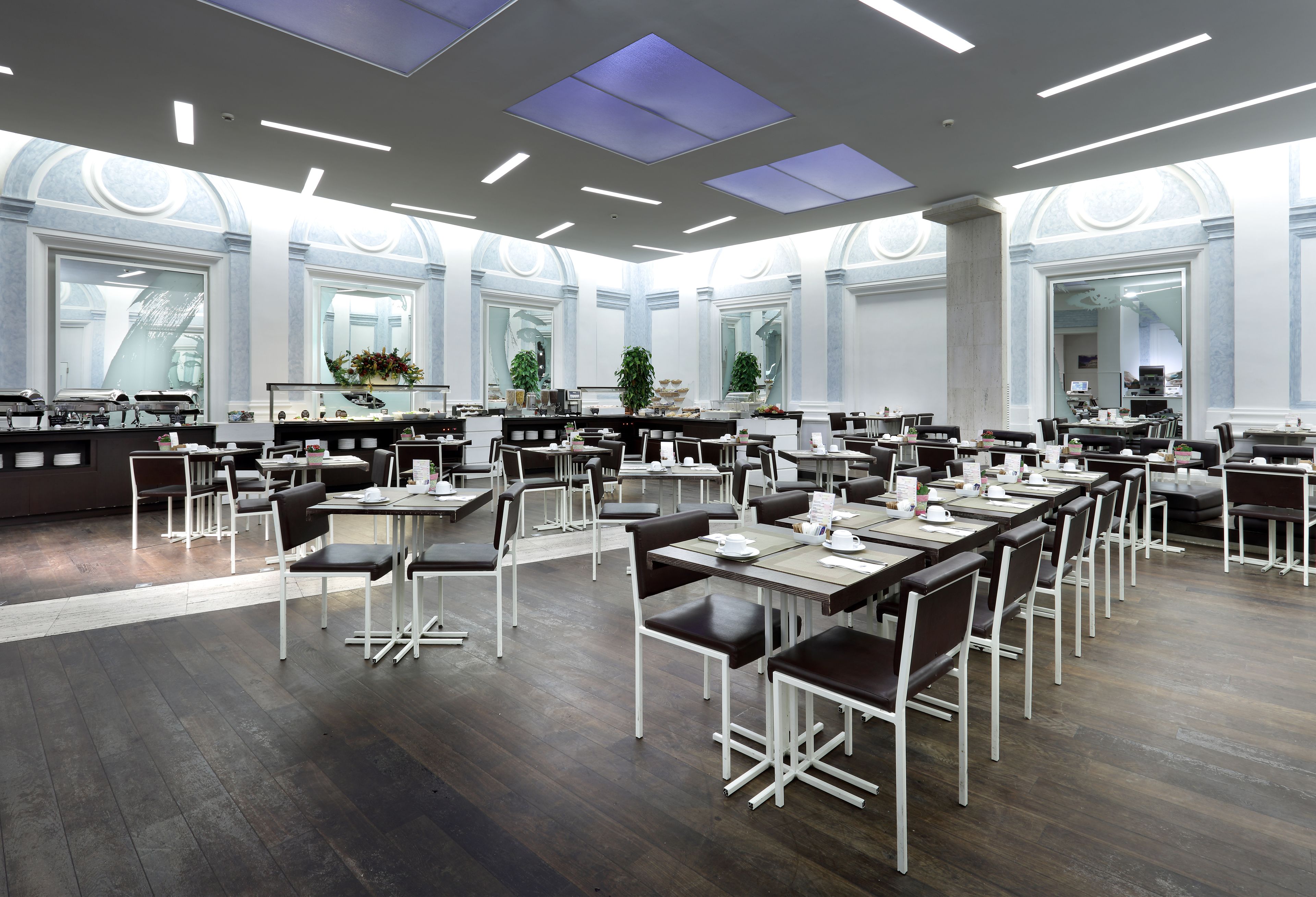 Un comedor espacioso con varias mesas y sillas, ventanas amplias y un diseño de techo moderno.