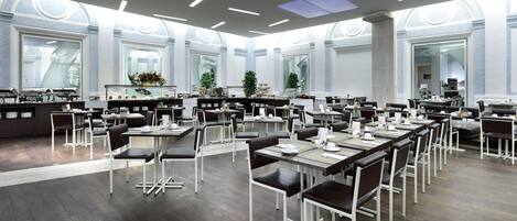 Un comedor espacioso con varias mesas y sillas, ventanas amplias y un diseño de techo moderno.