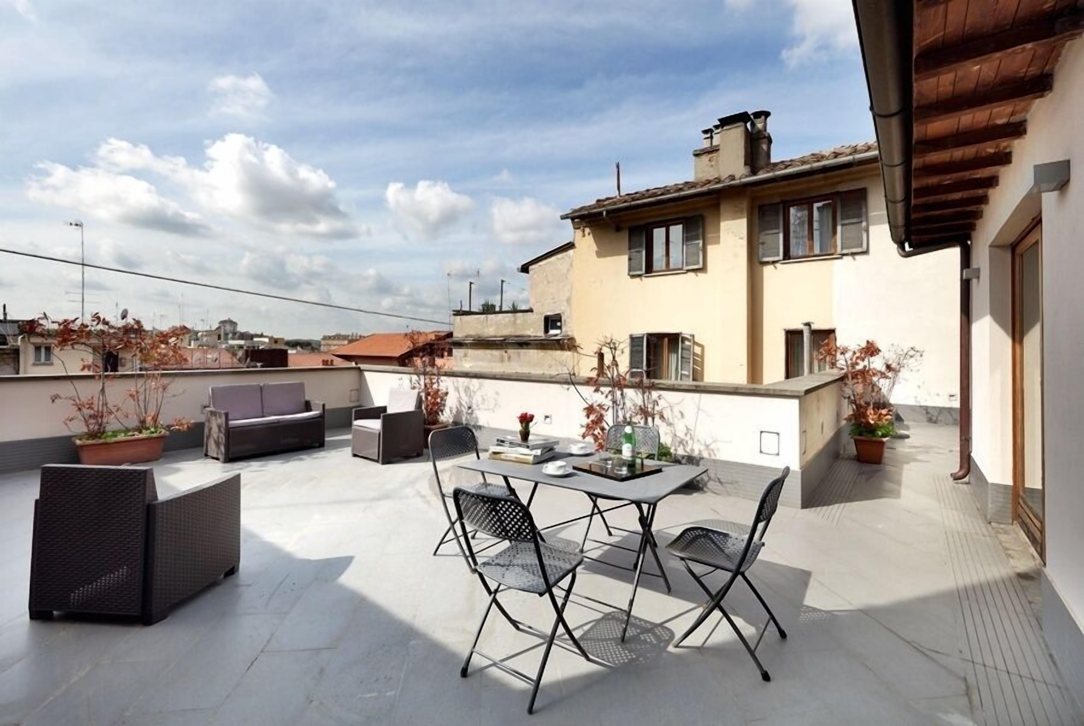 Una terrazza sul tetto con un tavolo da pranzo, sedie e piante in vaso.