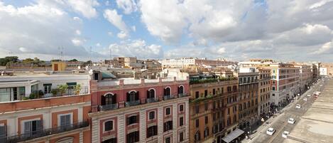 Una hilera de edificios de varios pisos con balcones, cielo despejado y una calle con automóviles.