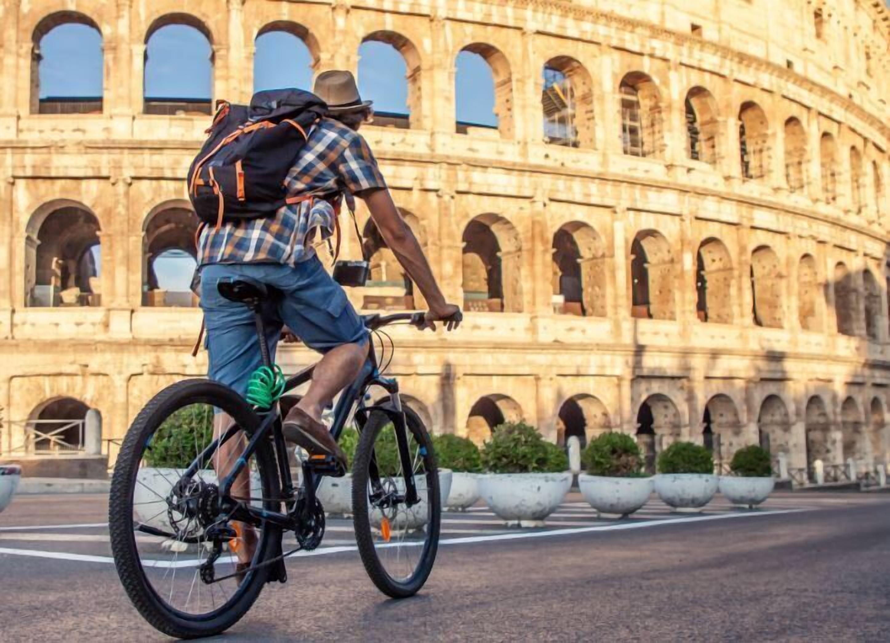 A person riding a bicycle with a backpack in front of the Colosseum.