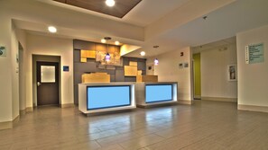 Un espace d’accueil au design moderne, comprenant un comptoir d’accueil, un écran numérique et un escalier menant aux chambres.
