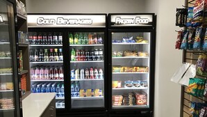 Un petit espace clos comprenant deux distributeurs de boissons réfrigérés, étiquetés « Boissons froides » et « Aliments surgelés », et un présentoir de collations situé à droite.