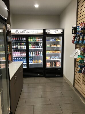 Un petit espace clos comprenant deux distributeurs de boissons réfrigérés, étiquetés « Boissons froides » et « Aliments surgelés », et un présentoir de collations situé à droite.