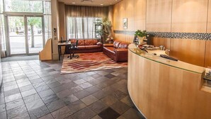 Un vestíbulo de hotel con mostrador de recepción, sofás de cuero, alfombra estampada y un gran ventanal con cortinas.