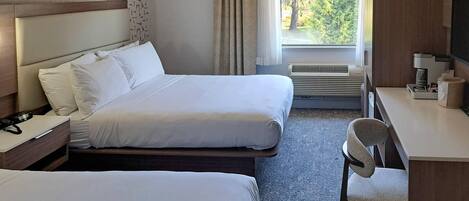 A hotel room with two beds, a desk, a chair, a TV, and a window with a view of trees.