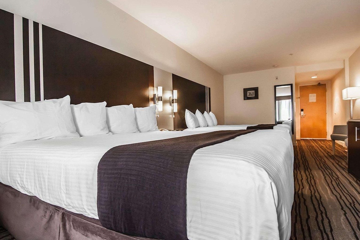 Une chambre d’hôtel avec un grand lit, une tête de lit sombre, des lampes fixées au mur et un sol recouvert de moquette.