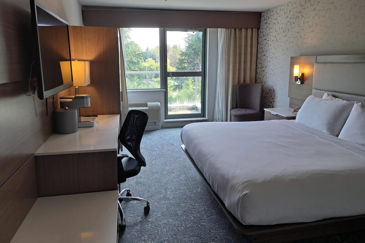 Une chambre d’hôtel avec un grand lit, un bureau avec une lampe, une chaise, une télévision et une fenêtre avec des rideaux.