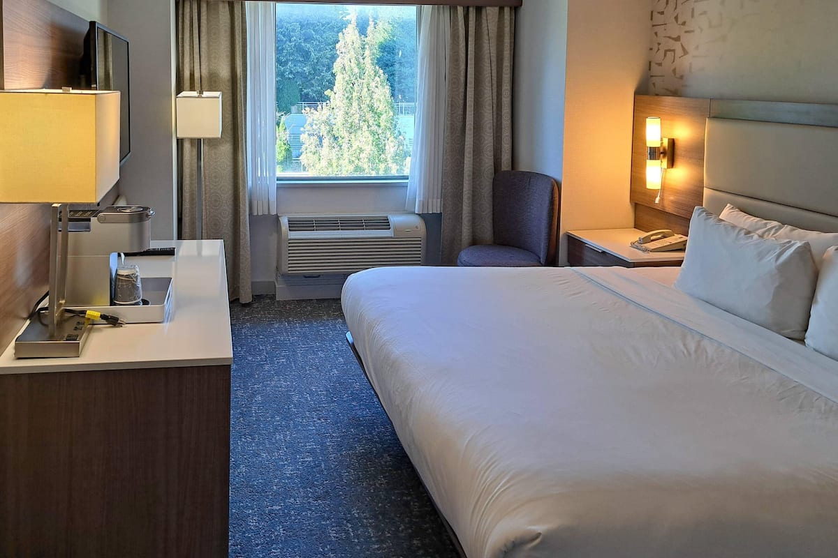 Une chambre d’hôtel avec un lit, un bureau, une chaise et une fenêtre avec des rideaux.
