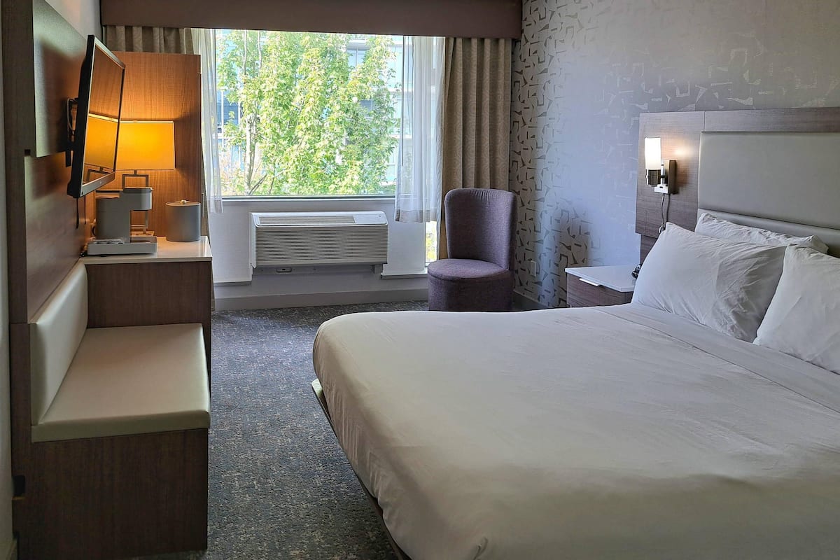 Une chambre d’hôtel avec un lit, un bureau avec une lampe, une chaise et une fenêtre avec des rideaux.