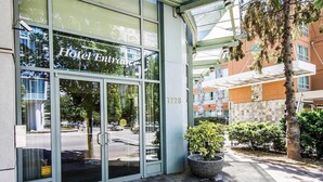 Entrada de hotel con puerta de cristal, número de fachada y un pequeño espacio exterior con una planta en maceta.