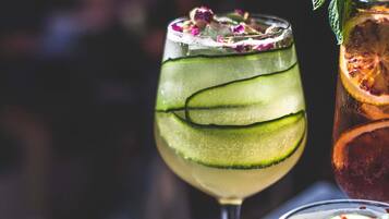 Un vaso de cóctel con rodajas de pepino y una ramita de menta, y otro vaso con un líquido oscuro y una rodaja de cítricos.