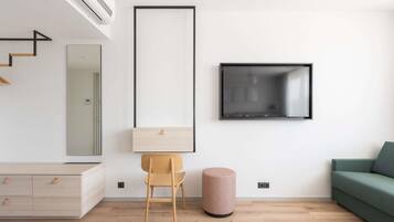Una sala de estar moderna con suelo de madera, un sofá verde, una silla de madera, un reposapiés redondo pequeño, un televisor montado en la pared y un diseño minimalista.
