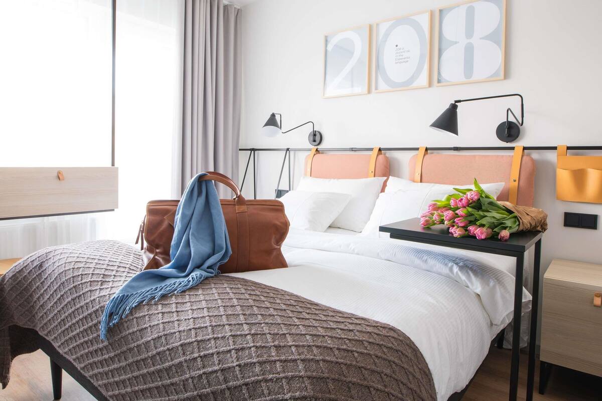 A modern bedroom with a bed, bedside tables, a lamp, a suitcase, and a wall with framed numbers.