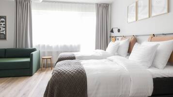 Camera d'albergo moderna con un letto grande, un divano verde, un tavolino e un'ampia finestra con tende.