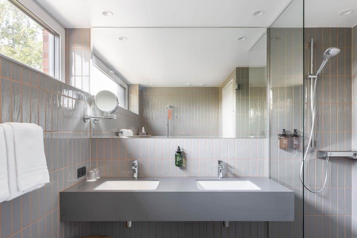 Ein modernes Badezimmer mit zwei Waschbecken, einem Spiegel, einer Dusche und einem Fenster.