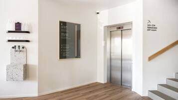 Un ascensor moderno con pantalla digital, una escalera con barandillas de madera y un cartel en la pared.