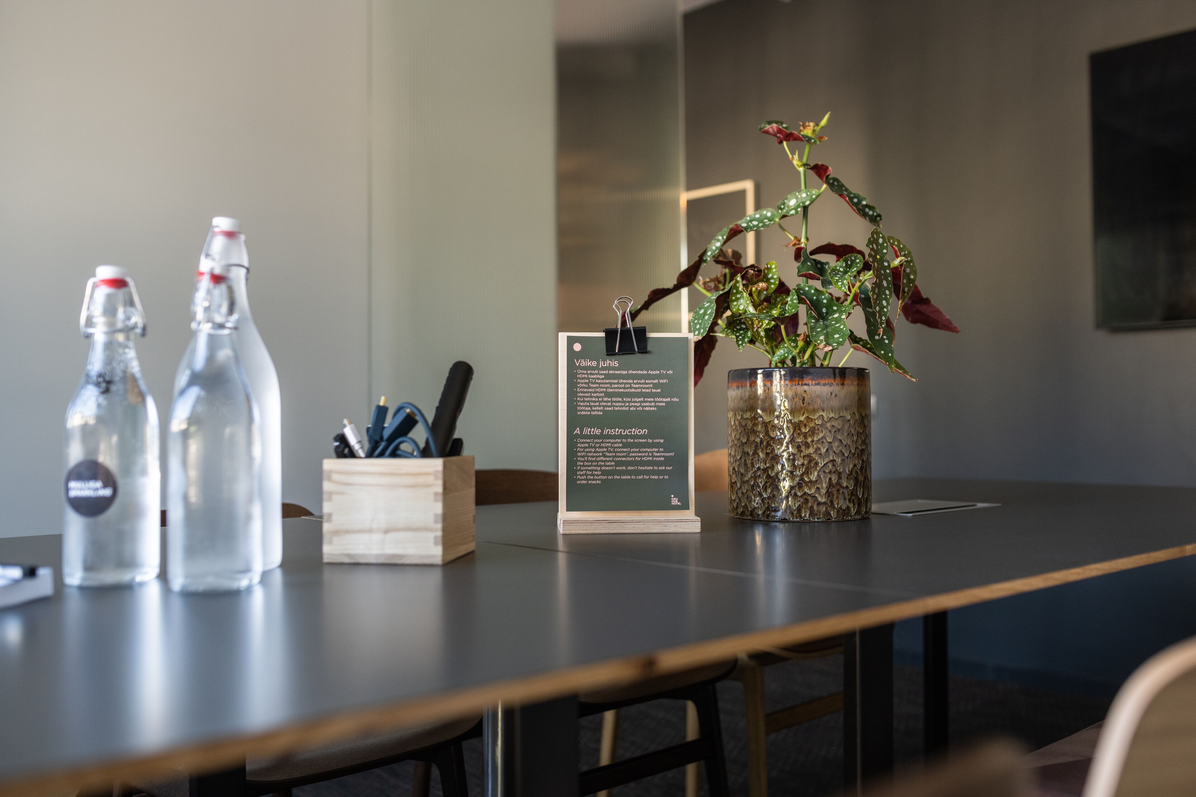 Een tafel met twee glazen flessen, een houten blokje met pennen, een potplant en een bord met instructies.