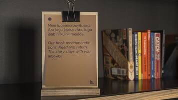Ein Buchtipp-Schild mit Holzfuß und Metallclip, platziert auf einem Regal mit einer Reihe Bücher im Hintergrund.