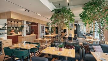 A modern restaurant interior with wooden tables, green chairs, and large potted plants.