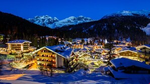 A snow-covered mountain town at night with illuminated buildings and a view of snow-capped peaks in the background. - Hotel Pinzolo Dolomiti (Pinzolo)