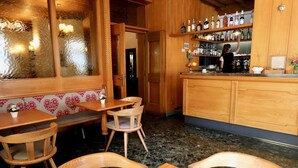 A cozy bar area with wooden furniture, a bar counter with various bottles, and a seating area with a patterned wall. - Hotel Pinzolo Dolomiti (Pinzolo)