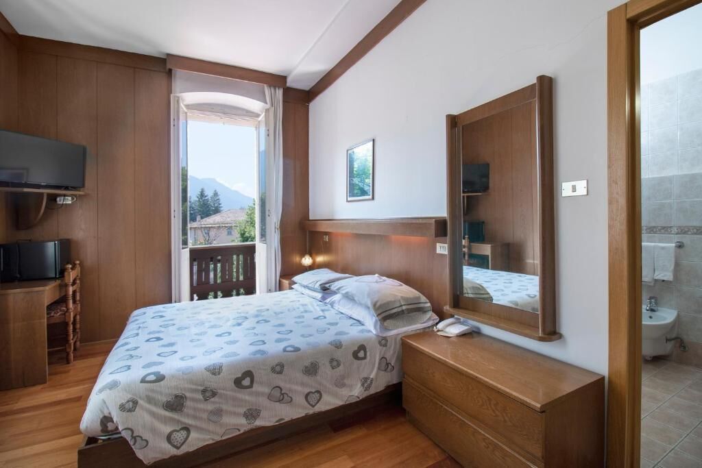 Un dormitorio con cama, mesita de noche, televisor y vistas al exterior.