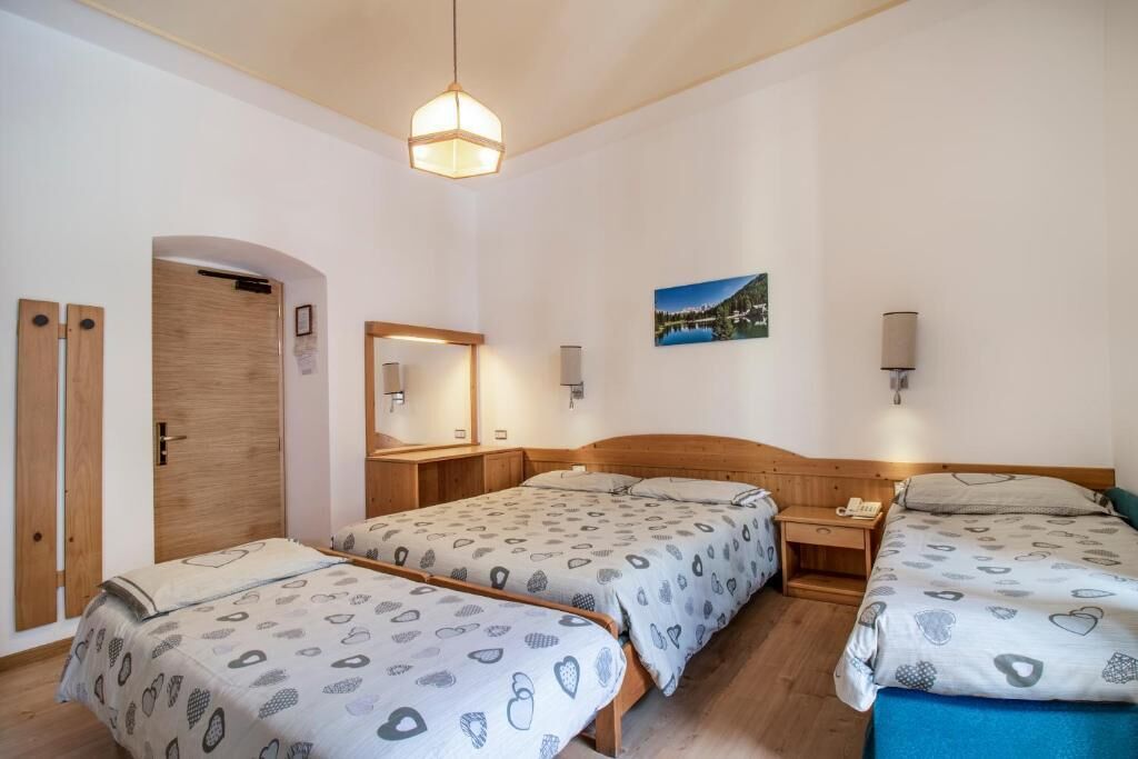 A hotel room with two beds, a wooden door, a mirror, a picture on the wall, and a bedside table with a lamp.