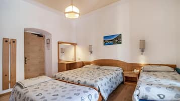 A hotel room with two beds, a wooden door, a mirror, a picture on the wall, and a bedside table with a lamp.
