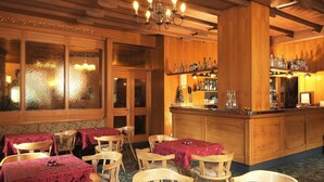 A cozy restaurant with wooden interiors, a bar area with bottles, and tables set with red tablecloths. - Hotel Pinzolo Dolomiti (Pinzolo)