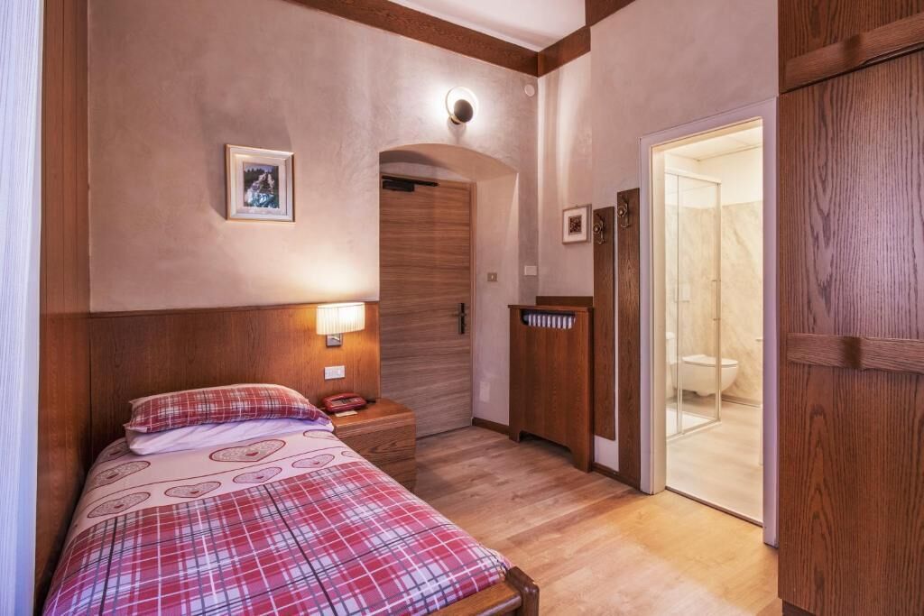 A bedroom with a bed, bedside table, lamp, and a door leading to a bathroom.