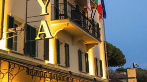 A building with balconies, a sign with illuminated letters, and flags. - Hotel Goya (Forte dei Marmi)