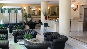 A lobby with black leather sofas, a reception desk, and a large mirror. - Hotel Goya (Forte dei Marmi)
