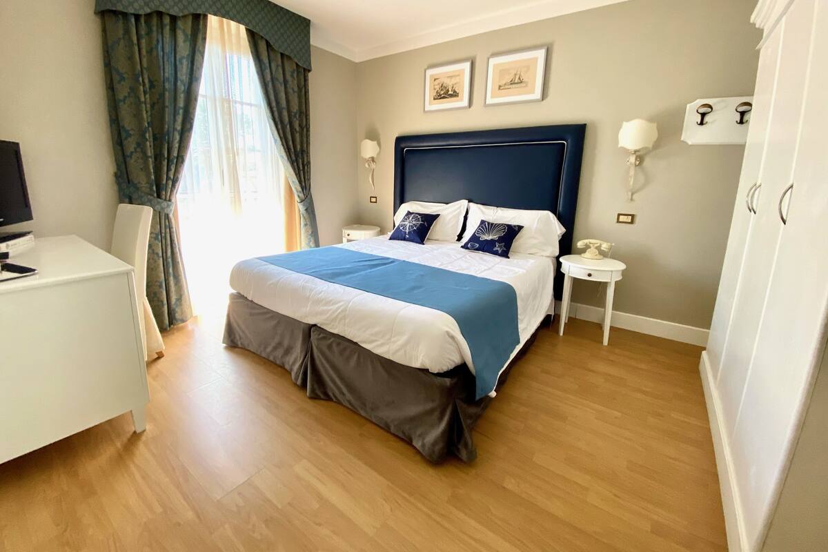 A neatly arranged bedroom with a bed, bedside tables, a desk, and a television.