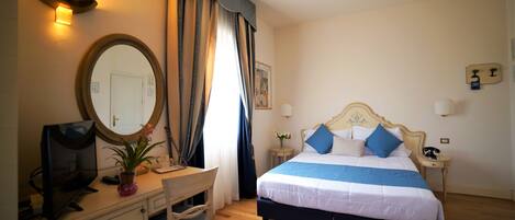 Habitación de hotel con cama, escritorio con computadora, silla, mesita de noche y espejo.