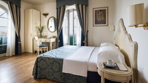A hotel room with a bed, a desk, a chair, a small table with a cup and a menu, and a window with curtains. - Hotel Goya (Forte dei Marmi)