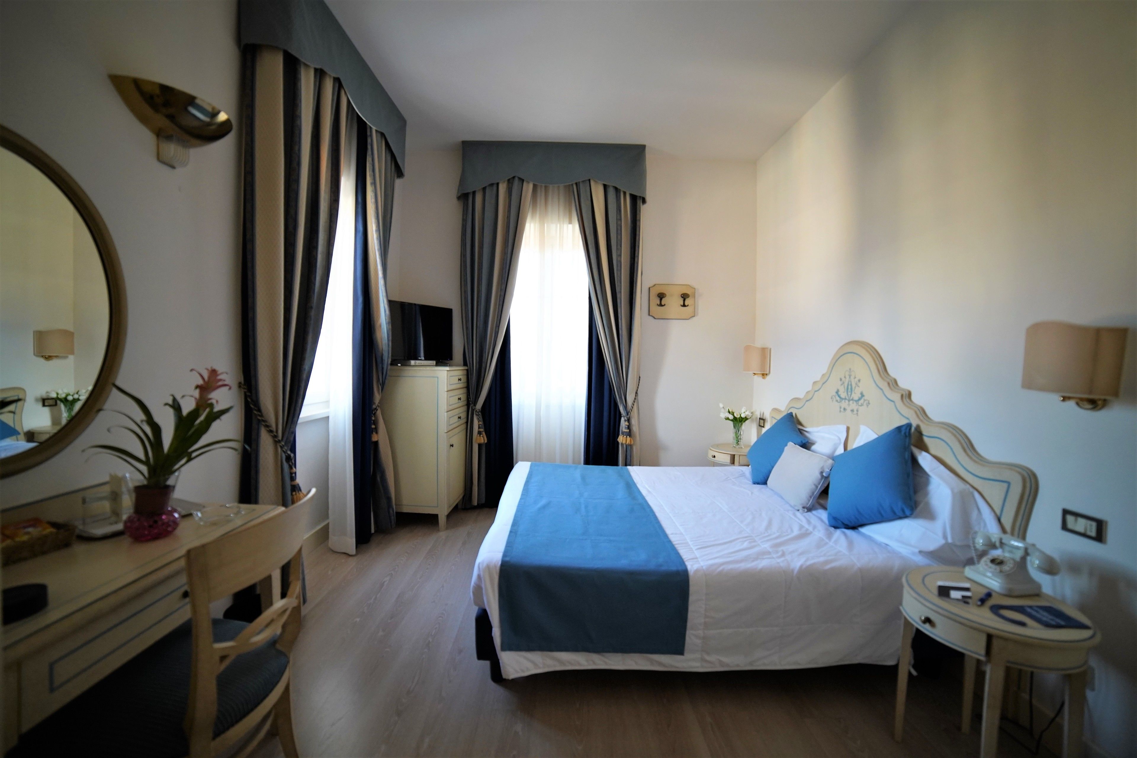 Quarto de hotel com cama, mesa de cabeceira, luminária e escrivaninha com cadeira.