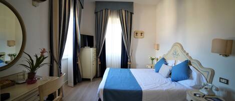 A hotel room with a bed, bedside table, lamp, and a desk with a chair.