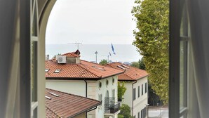 A view through an arched window of a coastal street with buildings, a tree, and parked cars. - Hotel Goya (Forte dei Marmi)