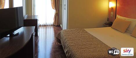 Quarto de hotel com cama, escrivaninha e televisão.